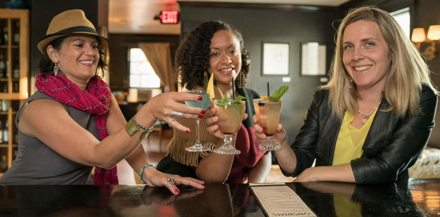 Women toasting cocktail glasses at bar